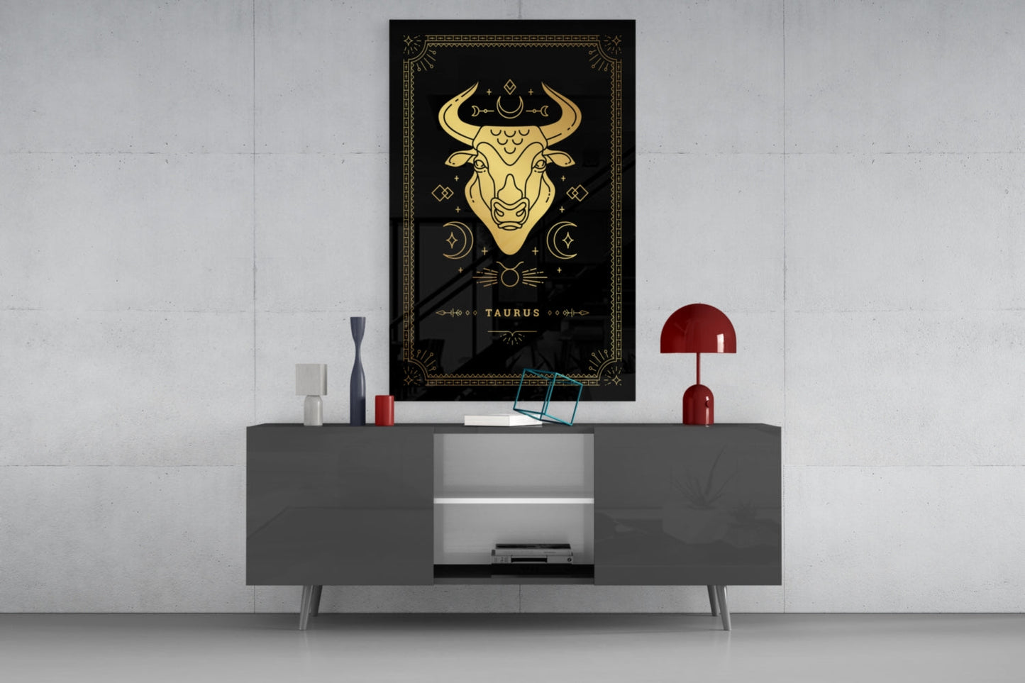 Black glass wall art featuring gold Taurus zodiac bull design displayed above gray console table with red lamp and decorative accessories.