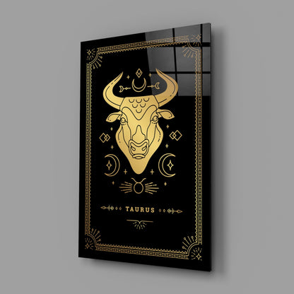 Angled three-quarter view of black glass wall art featuring gold Taurus zodiac bull head design with celestial symbols and decorative border.