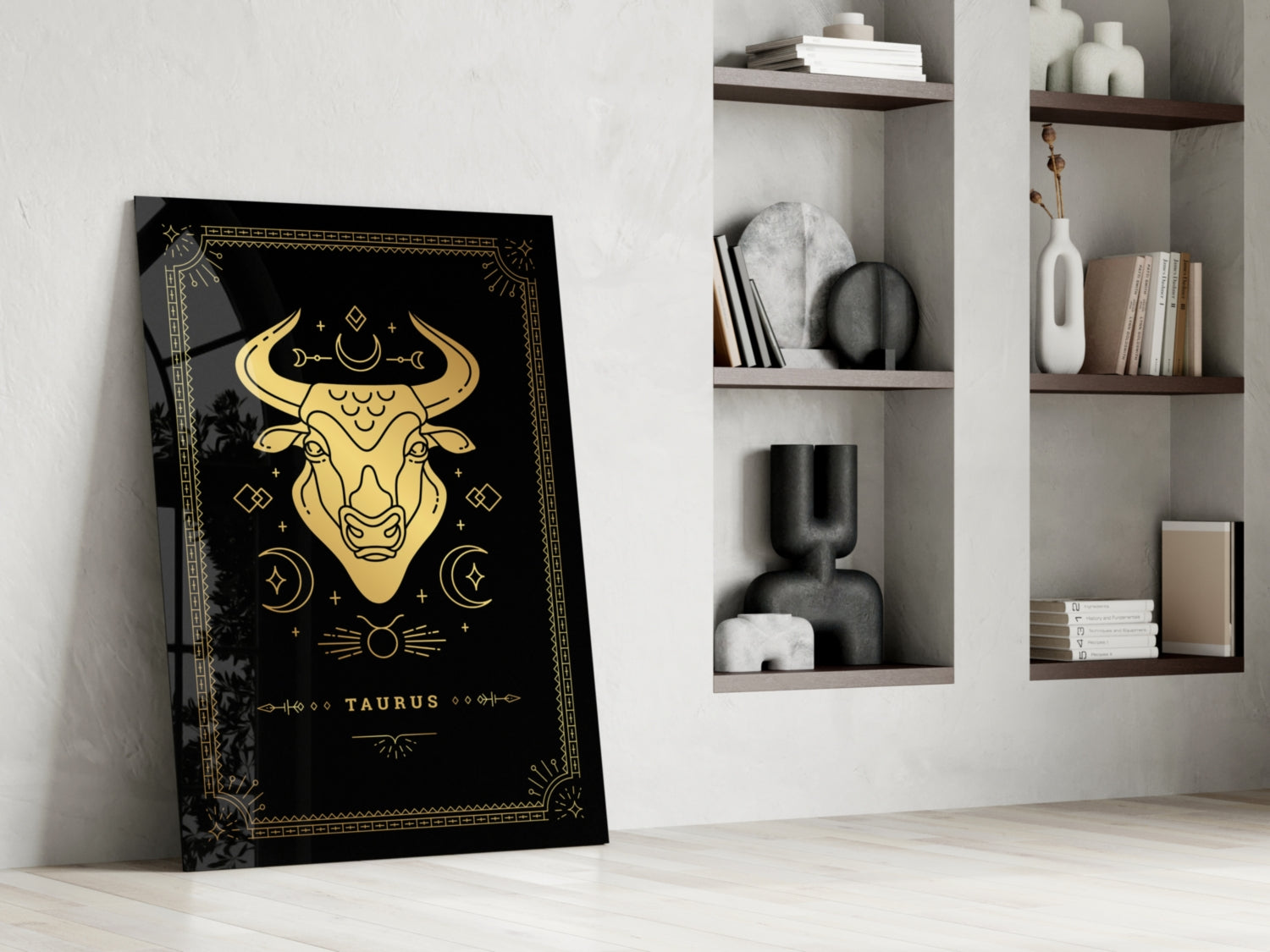 Black Taurus glass wall art with gold zodiac bull illustration leaning against white wall beside shelving unit.
