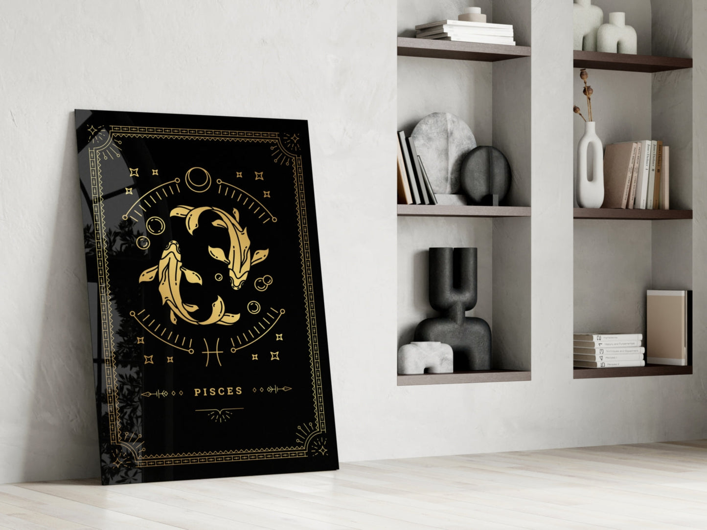 Black glass Pisces zodiac art leaning against white wall beside wooden shelving with decorative objects and books.