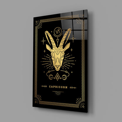 Angled perspective view of black glass wall art featuring gold Capricorn zodiac goat head design with decorative border and text.