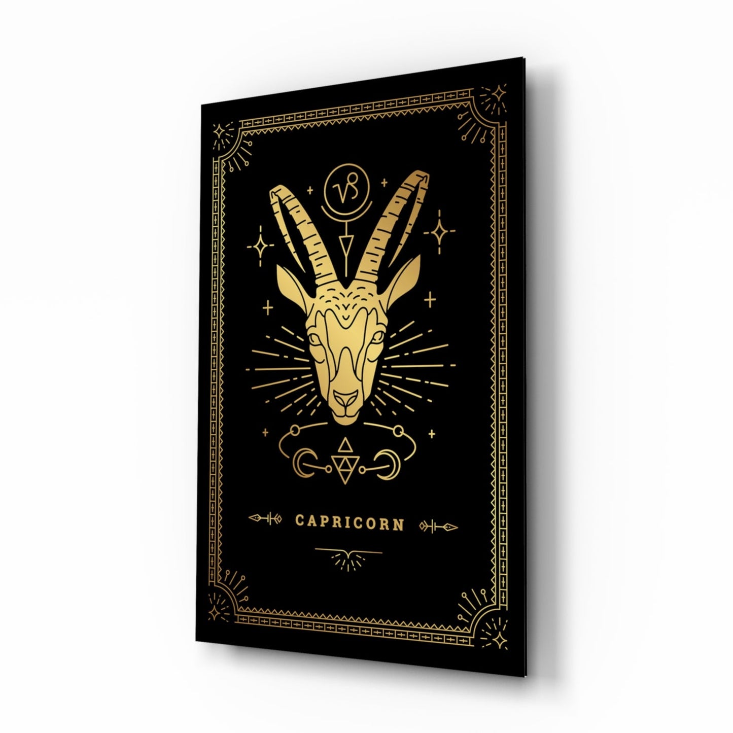 Angled 3/4 view of black glass wall art with gold Capricorn goat illustration and decorative border.