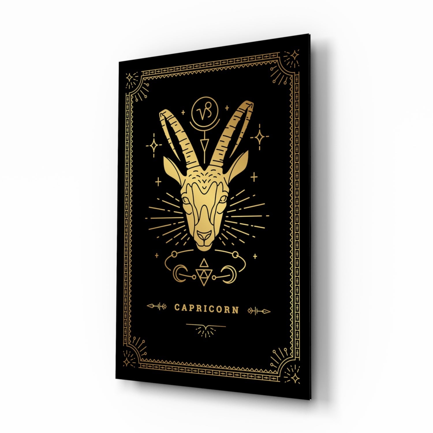 Angled 3/4 view of black glass wall art with gold Capricorn goat illustration and decorative border.