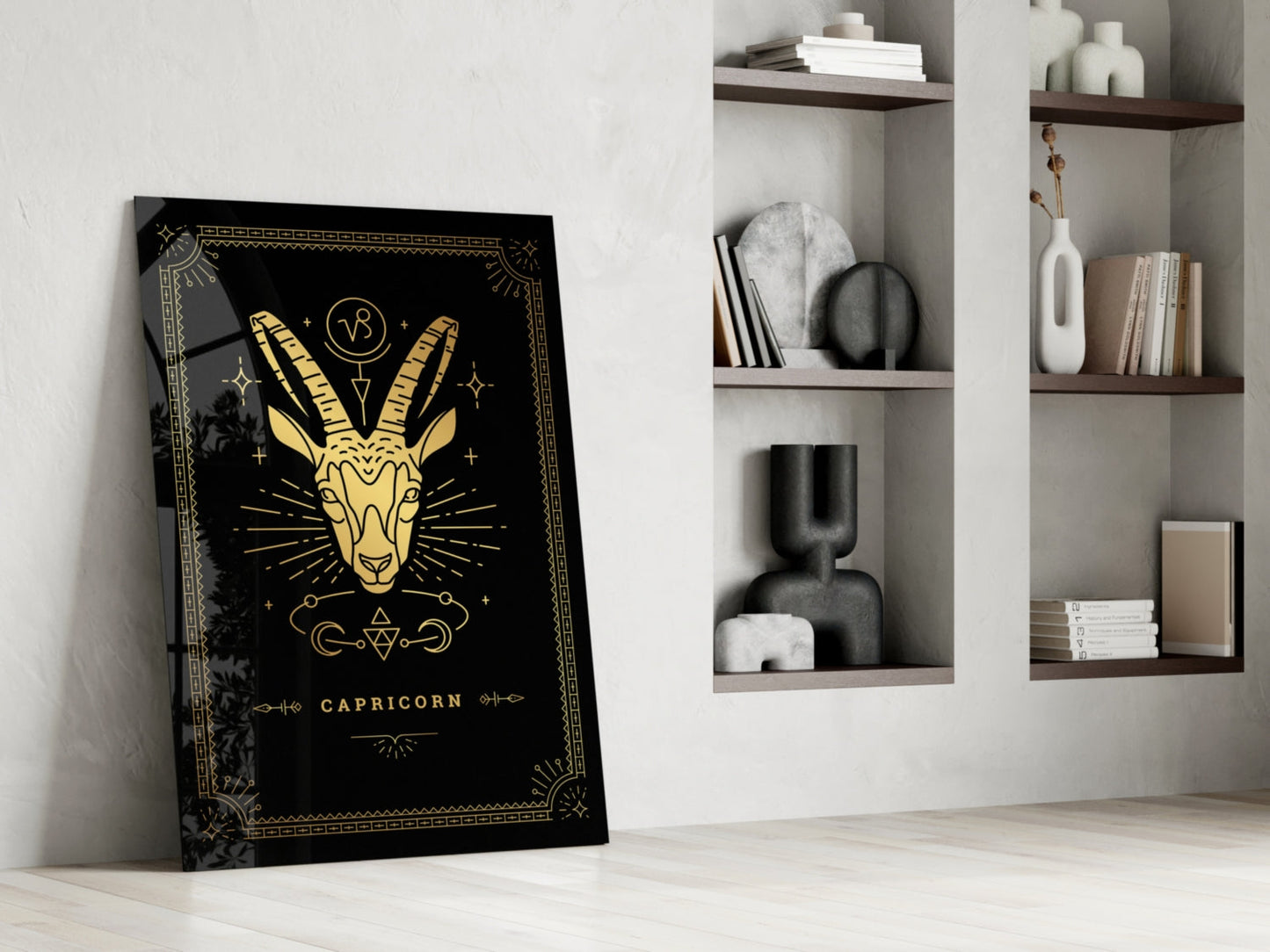 Black and gold Capricorn zodiac glass art leaning against white wall beside shelving unit.
