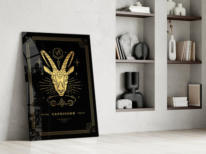 Black and gold Capricorn zodiac glass art leaning against white wall beside shelving unit.