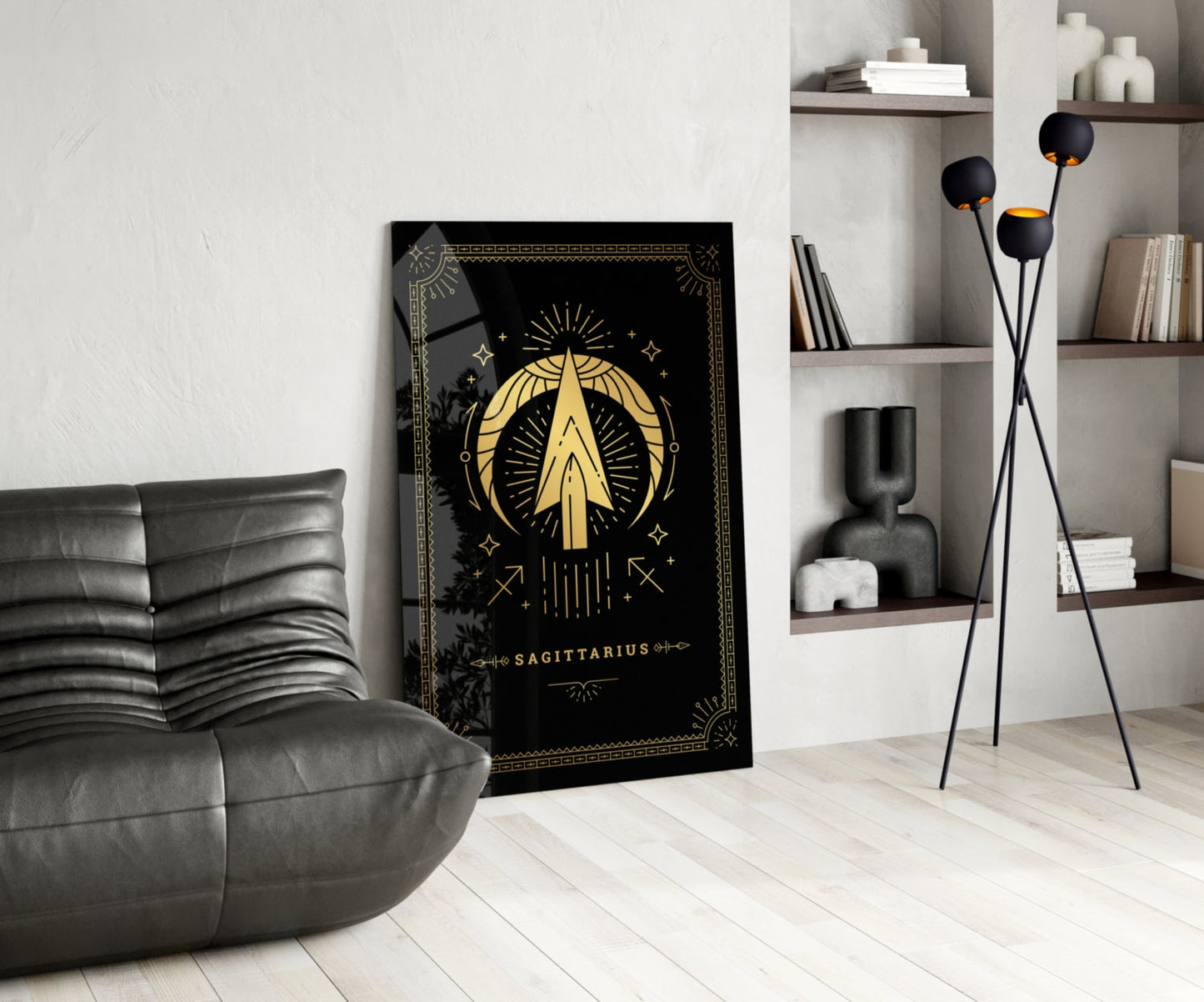 Black glass Sagittarius zodiac wall art with gold celestial design displayed in modern living room beside gray leather chair and shelving unit.