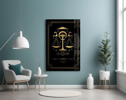 Libra zodiac glass wall art with gold scales on black background displayed in modern living room with teal walls, white chair, and potted plants.