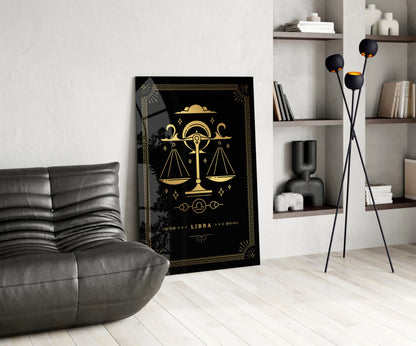 Black glass Libra zodiac wall art with gold scales and celestial design displayed in modern living room next to gray chair and shelving.