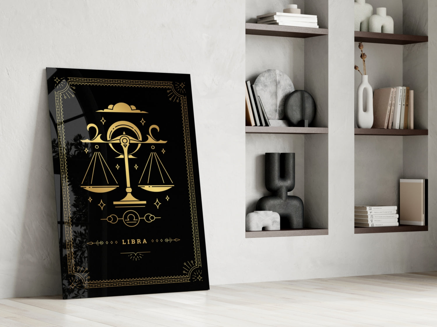 Black glass Libra zodiac wall art with gold scales and celestial symbols leaning against white wall beside shelving unit.